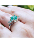2.18 ct cushion cut emerald ring with trillion side diamonds on a hand, 14K white gold.