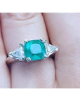 Emerald ring with trillion side diamond accents made in 14k white gold on a finger.