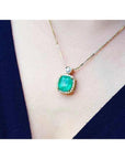 Cushion cut emerald necklace in 18K yellow gold with diamond halo and solitaire, worn on a person.