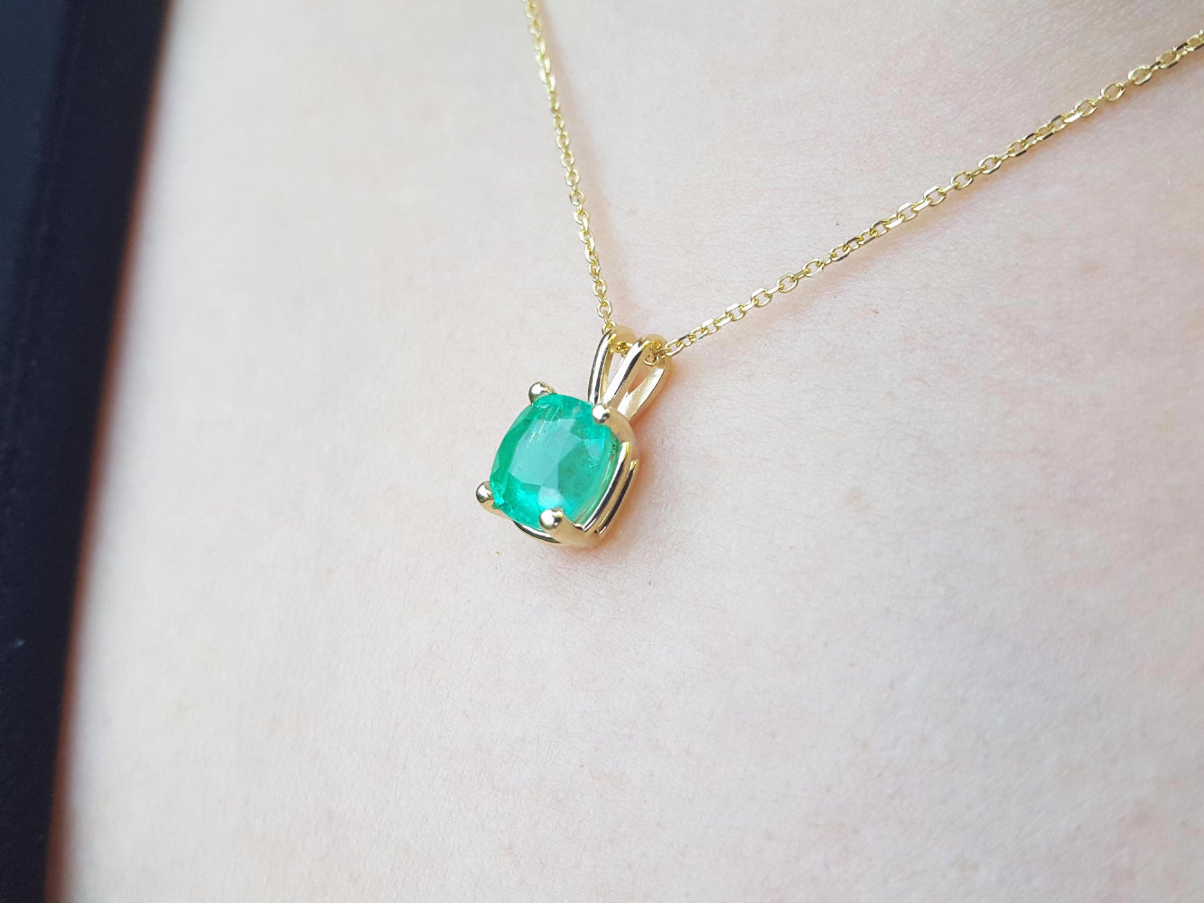 A 14k yellow gold emerald solitaire pendant on a woman's neck.