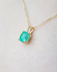 A 14k yellow gold emerald solitaire pendant on a woman's neck.