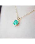 Cushion cut natural emerald solitaire pendant in 14K yellow gold, worn on a neck.