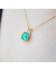 Cushion cut natural emerald solitaire pendant in 14K yellow gold, worn on a neck.