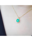 Cushion cut natural emerald solitaire pendant in 14K yellow gold, worn on a neck.