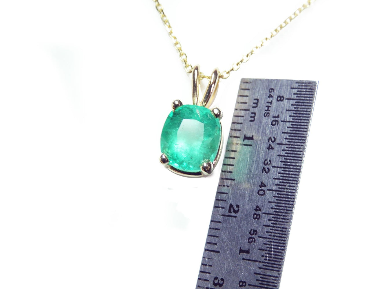 A yellow gold natural emerald solitaire pendant next to a ruler on a white background.