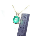 Cushion cut natural emerald solitaire pendant in 14K yellow gold with ruler for scale.