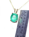 A yellow gold natural emerald solitaire pendant next to a ruler on a white background.
