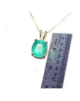 Cushion cut natural emerald solitaire pendant in 14K yellow gold with ruler for scale.