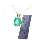 Cushion cut natural emerald solitaire pendant in 14K yellow gold with ruler for scale.