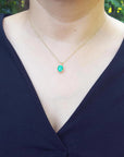 A woman wearing a necklace with a cushion emerald pendant against a blurred green background.