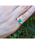 1.47 ct. emerald-cut Colombian emerald ring with trillion diamonds in 18k yellow gold on a hand.