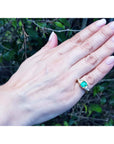 Hand wearing a gold ring with a natural colombian emerald and trillion diamonds against a natural background.