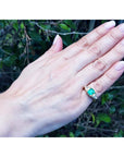 Hand wearing a gold ring with a natural colombian emerald and trillion diamonds against a natural background.