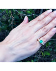 1.47 ct. emerald-cut Colombian emerald ring with trillion diamonds in 18k yellow gold on a hand.