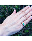 1.47 ct. emerald-cut Colombian emerald ring with trillion diamonds in 18k yellow gold on a hand.