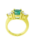 A lateral view of a 18k yellow gold emerald and trillion diamonds ring for women