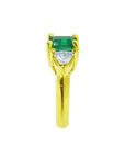The 18k yellow gold natural colombian emerald and trillion diamonds ring for women in a side profile view.