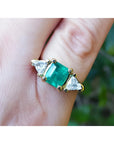 Women's ring with a center natural colombian emerald and two trillion side diamonds, crafted in 18k yellow gold.