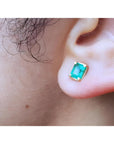 An earlobe wearing a natural colombian emerald stud earring in 14k yellow gold.