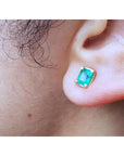 An earlobe wearing a natural colombian emerald stud earring in 14k yellow gold.
