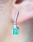 Close-up of an emerald dangle earring on a person's ear.