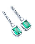 Pair of emerald dangle earrings with 14k white gold settings right side position top view