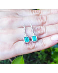 Pair of emerald-cut gemstone earrings held in a hand with a natural background