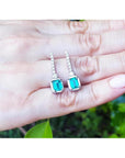 18K white gold dangling emerald-cut emerald earrings with diamond-studded lines.