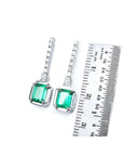 18K white gold dangling earrings with emerald-cut Colombian emeralds and diamond studs, shown with ruler.