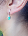 Close-up of a real Colombia emerald earring on a person's ear with a blurred natural background