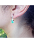 Close-up of a real Colombia emerald earring on a person's ear with a blurred natural background