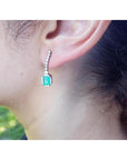 Close-up of a real Colombia emerald earring on a person's ear with a blurred natural background