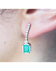 Close-up of a natural colombian emerald dangle earring with diamonds on a person's ear.
