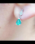 Close-up of an emerald and diamond teardrop earring in white gold on a woman's ear.