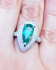 esmeralda colombiana corte pera con diamantes natural en oro blanco exhibido en una mano.