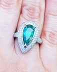 esmeralda colombiana corte pera con diamantes natural en oro blanco exhibido en una mano.