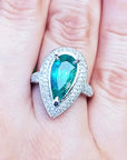 esmeralda colombiana corte pera con diamantes natural en oro blanco exhibido en una mano.