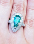 esmeralda colombiana corte pera con diamantes natural en oro blanco exhibido en una mano.