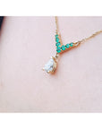 14K gold necklace with a pear-cut diamond pendant and V-shaped emerald centerpiece, shown worn on a person's neck.