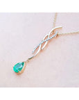 14K yellow gold twisted slider necklace with a pear-shaped emerald and diamond accents, displayed on a light pink background.