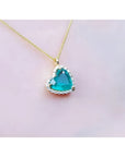 Tilted heart emerald pendant with halo diamonds on an 18K yellow gold chain.