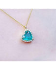Tilted heart emerald pendant with halo diamonds on an 18K yellow gold chain.