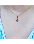 Teardrop-shaped blue opal pendant on a gold chain worn by a person with a blue and white patterned top.