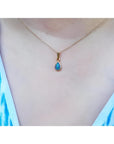 Pear-shaped doublet opal pendant with bluish-green sparkles, bezel set in 14K yellow gold on a delicate chain.