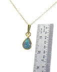 Pear-shaped doublet opal pendant with bluish-green sparkle, bezel set in 14K yellow gold on a chain, next to a ruler.