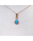 Pear-shaped Australian doublet opal pendant with bluish-green sparkle, bezel set in 14K yellow gold on a chain.