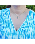 Pear-shaped Australian doublet opal pendant with bluish-green sparkles, bezel set in 14K yellow gold on a woman's neck.
