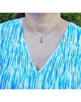 Pear-shaped Australian doublet opal pendant with bluish-green sparkles, bezel set in 14K yellow gold on a woman's neck.