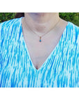 Pear-shaped Australian doublet opal pendant with bluish-green sparkles, bezel set in 14K yellow gold on a woman's neck.