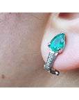 Close-up of a teardrop emerald earring clip-on system on an ear.